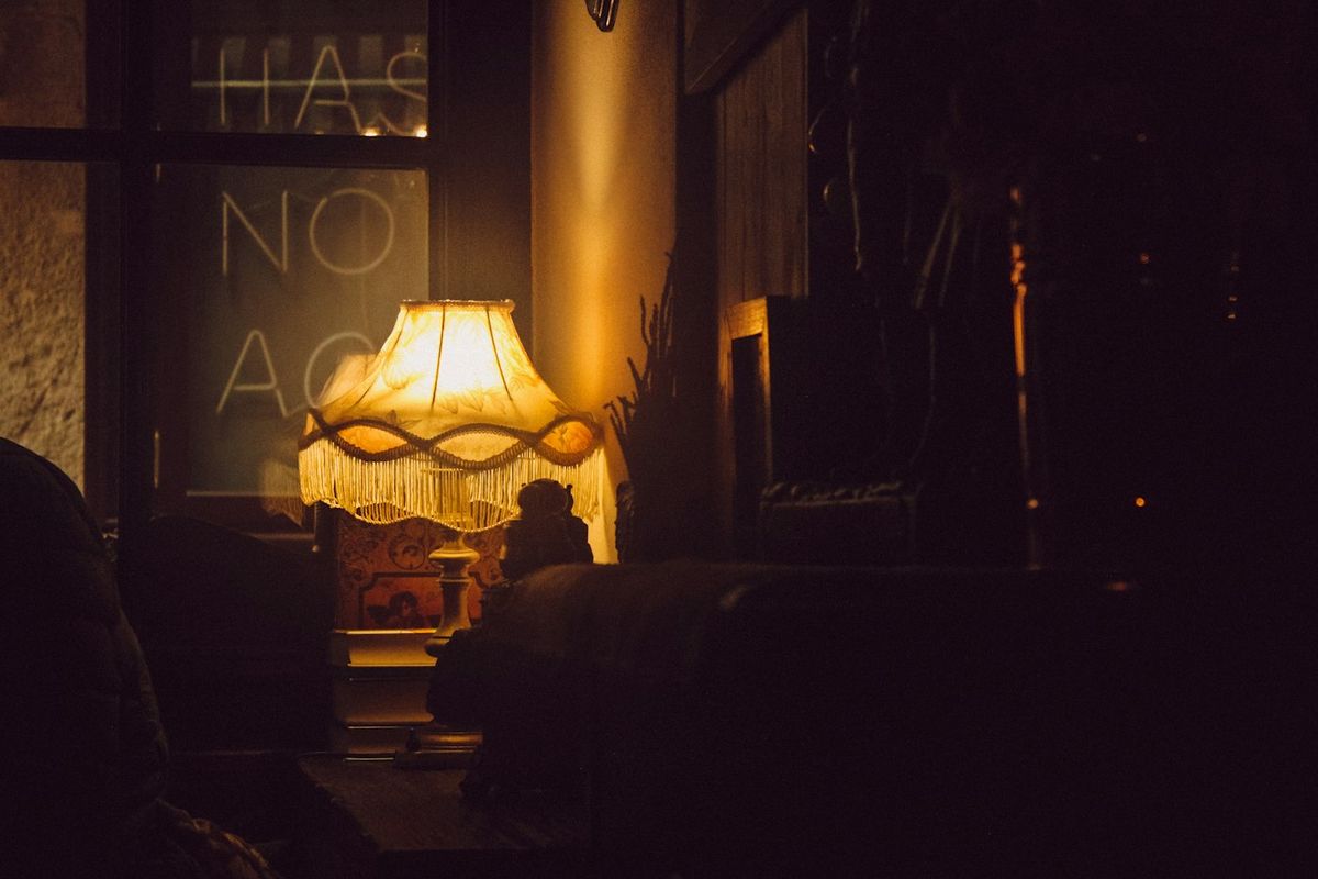 Bordslampa med fransar som lyser varmt i ett mörkt rum